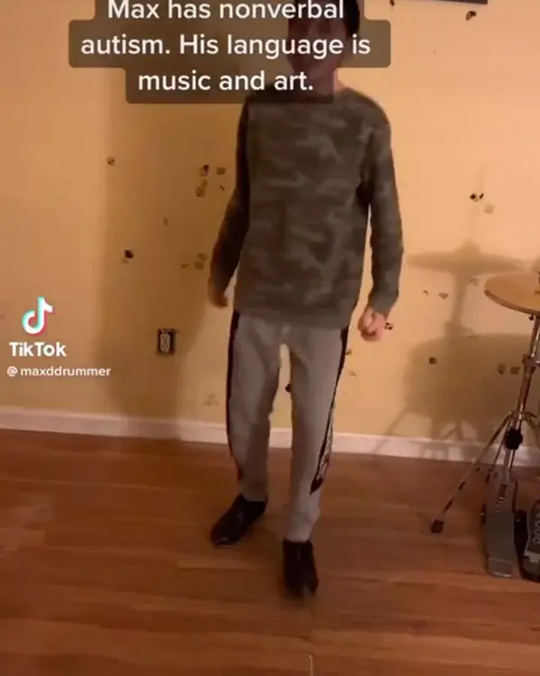 A young drummer standing in his room beside a drum kit.