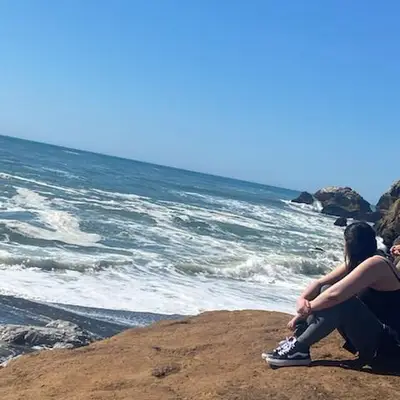 Yuvibaby sitting on rocks by the ocean.