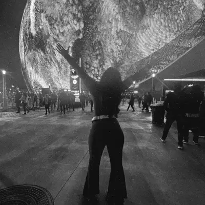 Yuvibaby with arms raised in front of the Las Vegas Sphere at night.