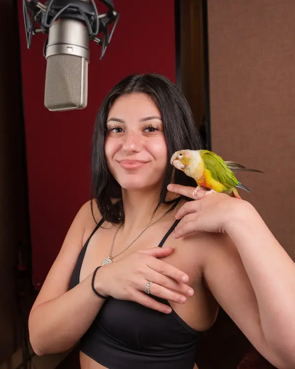 Yuvibaby in the studio with a green parrot on her shoulder.